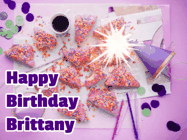 Happy Birthday Brittany GIF: A big paper sparkle highlights this animated birthday gif showing a birthday cake place setting with decorations.