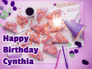 Happy Birthday Cynthia GIF: A big paper sparkle highlights this animated birthday gif showing a birthday cake place setting with decorations.