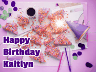 Happy Birthday Kaitlyn GIF: A big paper sparkle highlights this animated birthday gif showing a birthday cake place setting with decorations.