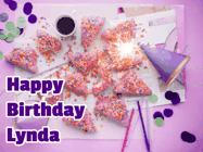 Happy Birthday Lynda GIF: A big paper sparkle highlights this animated birthday gif showing a birthday cake place setting with decorations.