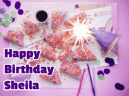 Happy Birthday Sheila GIF: A big paper sparkle highlights this animated birthday gif showing a birthday cake place setting with decorations.
