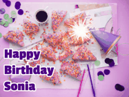 Happy Birthday Sonia GIF: A big paper sparkle highlights this animated birthday gif showing a birthday cake place setting with decorations.