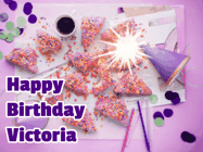 Happy Birthday Victoria GIF: A big paper sparkle highlights this animated birthday gif showing a birthday cake place setting with decorations.